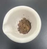 A photo of a mortar with a crushed-up, brown, dried leaf-like substance in it.