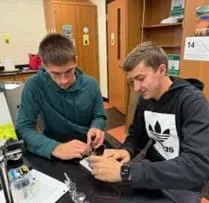A photo showing two high school students using a breadboard, wires, and other electrical components to build an integrated logic circuit.