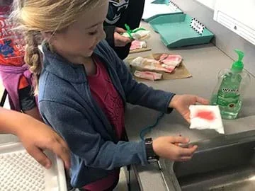 A girl holds a piece of medical gauze stained red with water mixed with red food coloring.
