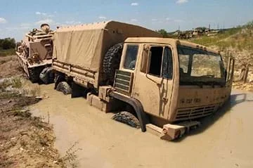 A brown military truck is stuck in deep mud.