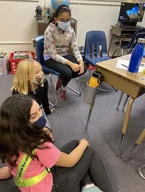 The final design of one team’s water bottle holder is shown attached to the leg of a desk with a large water bottle inside.