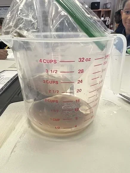 A small corner of the plastic bag was cut, and water was poured through the bag. Water drains through the soil and gets deposited in the measuring cup.