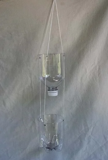 A soda bottle cut in half is hung from string.