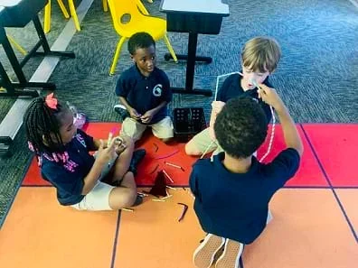 Four students are being observed manipulating straws and chenille sticks/pipe cleaners to create their design.