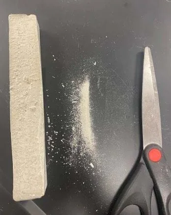 The image shows the solubility station. Scissors can be used to shave a small amount of the concrete sample into powder. This concrete powder can then be used to test if the concrete sample is soluble in water.