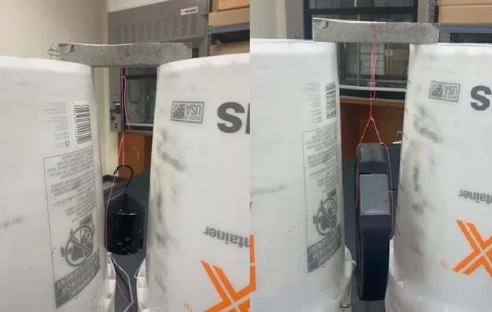 The image shows the strength test station. The buckets being used are holding up the concrete sample so that weights can be hung suspended around the sample to test how much weight the sample can hold up. A string is tied to the middle of the sample where a divot is made to hold the string in place and the weights are tied to the other end being held suspended by the concrete sample. The weights are increased until the concrete sample breaks. The image shows the sample holding up a 200g weight to the left and a 5 lb. weight on the right. Maximum weight added is 10lbs.