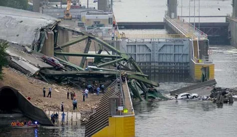 A photo shows the I-35 Mississippi River Bridge after its August 2007 collapse. The destroyed bridge is in the water with its on-land steel truss components twisted and broken.