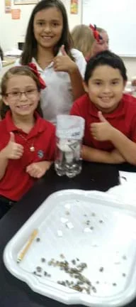 A photograph shows three young students holding their thumbs up in front of their water filtration system.