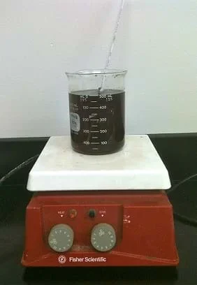 A photo show a beaker of dark brown liquid on hot plate with the heating dial turned to level 3 of 10.