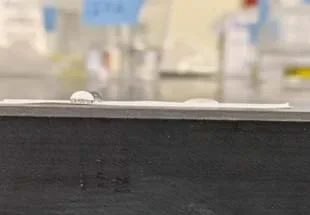 A photo showing a close-up of two pure water droplets and one soapy water droplet on a strip of Teflon tape.