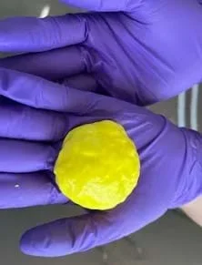 A photo showing gloved hands holding Controlled Slime (Accommodation) (10 g contact lens solution)