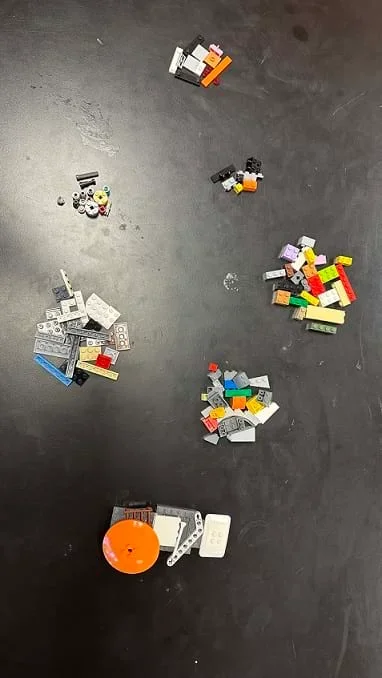 A photo showing various colors and shapes of LEGO pieces sorted and arranged into groups. There are seven groups of LEGO pieces on the table; the pieces within each pile look similar in size.