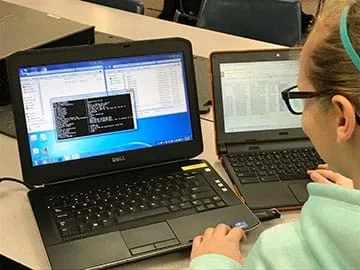 Young female with glasses looking at two laptop computers, analyzing exif metadata.