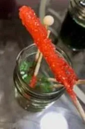A photo of the end result of the at-home experiment, including a red sugar rock candy in the first plane and four more sugar rock candies of different colors resting in a glass container.