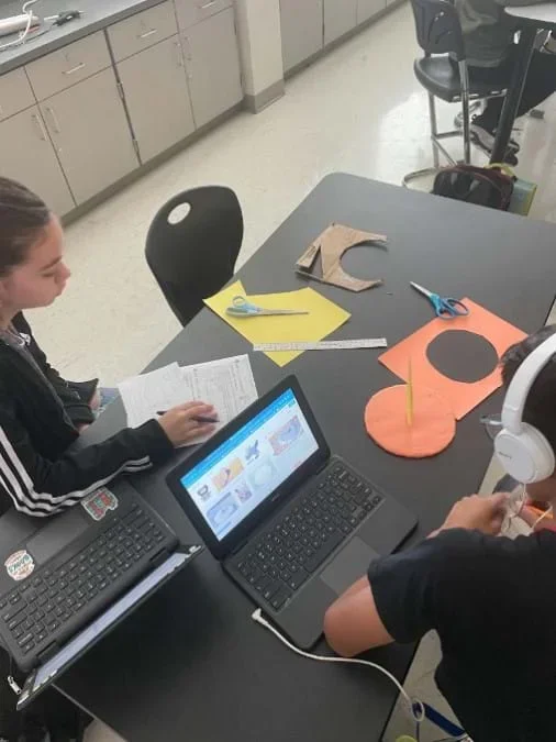 Two students check to see whether their sundial works by observing where the shadow falls after light is shined on it.