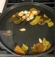 A photo of avocado skins, cut into pieces, boiling in a black pan filled with water on a stove.