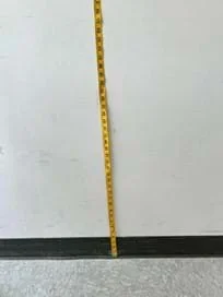 A photo showing a tape measure taped to the wall. The bottom of the tape measure is on the ground.