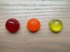 A photo showing a water solution gummy that is red, a sugar solution gummy that is orange, and a salt solution gummy that is yellow.
