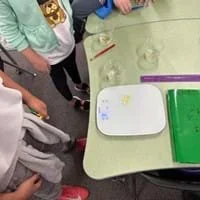 A photo showing three students measuring the length of a gummy with a gram scale.