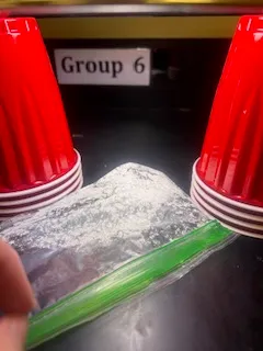 A photo of UV beads under 60 seconds of UV light exposure with a sample sunscreen in a plastic bag laid on top to test sunscreen efficacy.