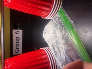 A photo of UV beads under 60 seconds of UV light exposure with a sample sunscreen in a plastic bag laid on top to test sunscreen efficacy.