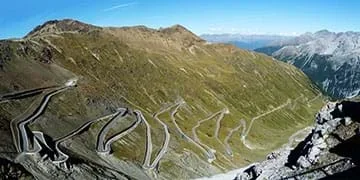 A photograph shows a winding road ascending through a valley and up a mountain. The road is made of several switchbacks that climb on top of each other, with large mountains in the background.