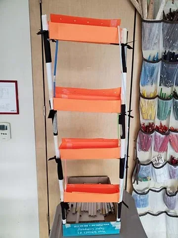 A student prototype of a hydroponics system hangs in a classroom. This design is a mock-up using paper materials.
