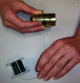 Photo shows a person's hands winding a coil of wire around a cylindrical battery.