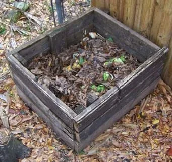 A photograph shows an open box made of boards sitting next to a fence outdoors, and partially filled with food scraps and leaves.