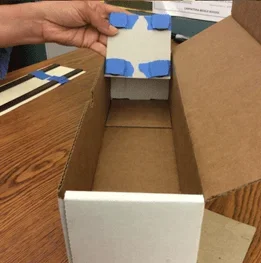A photo showing an example maglev train device, with four disk magnets taped to the corners of a square piece of cardboard.