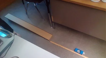 A photo showing an elevated wooden ramp with a meter stick on the floor at the bottom of the ramp. Halls cart with washers pushed the block at the end of the ramp.