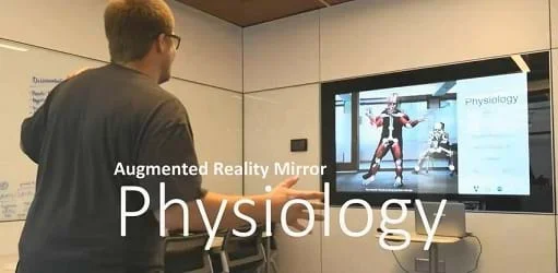 A photograph showing a person standing in front of a TV where the image on the TV is a mirrored picture of them with a muscle overlay.