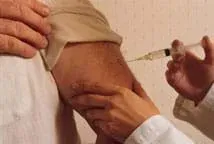 Photo shows hands injecting a syringe into a man's upper arm.