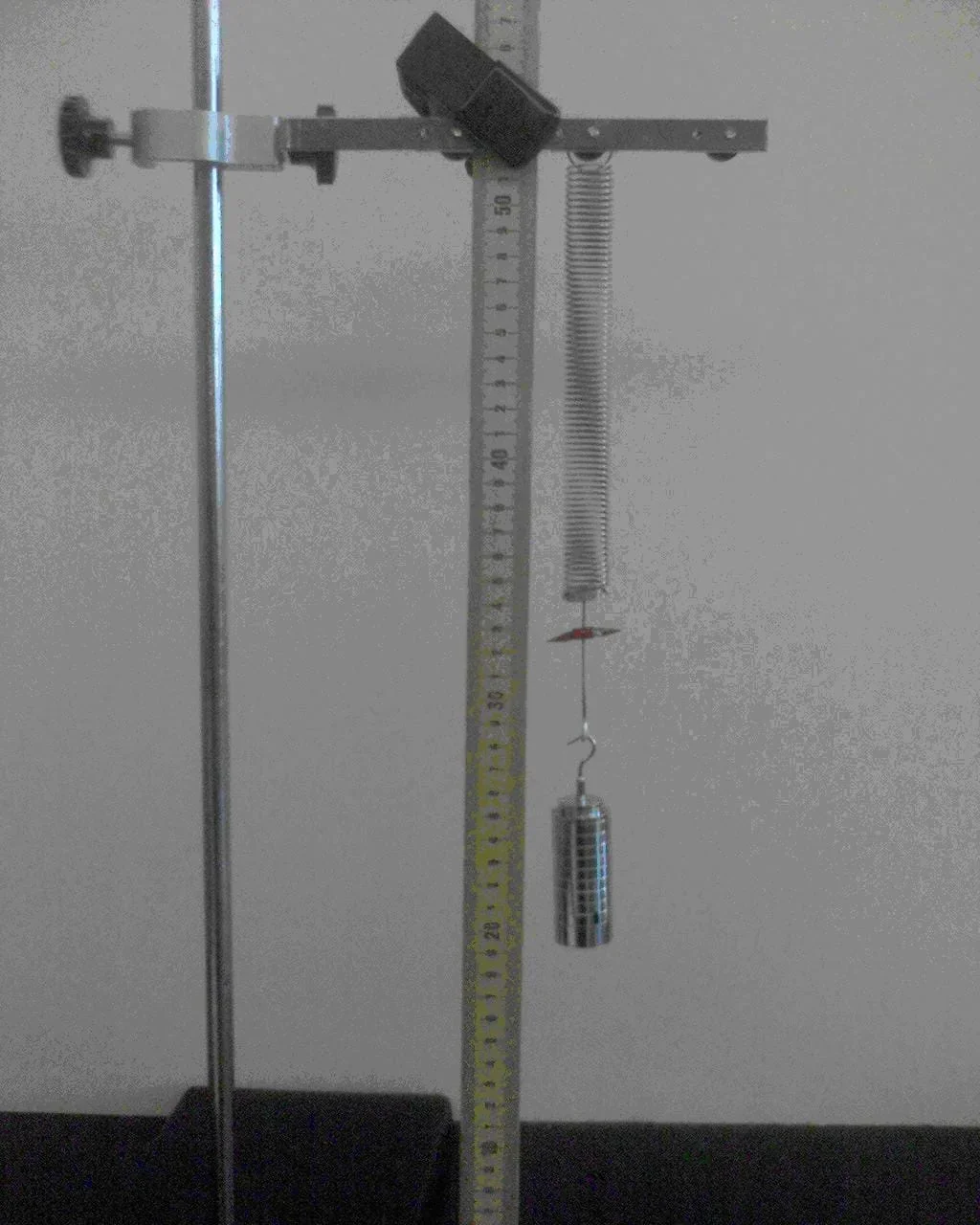 Photo shows a spring hanging from a lab stand with a vertical ruler positioned nearby.