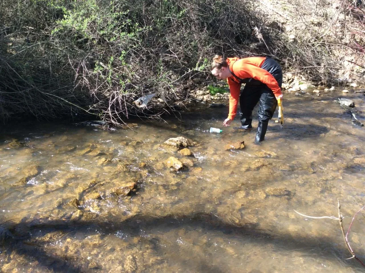 Two students stand in a stream and use measuring tape in a flow rate exercise.