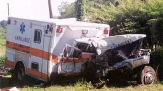 Photo shows an ambulance damaged from a crash. The front cab of the truck is crumpled and torn away from a dented back section.