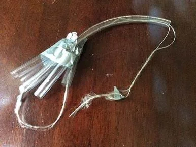 A photograph shows an assistive hand device prototype composed of a long piece of tubing attached by duct tape to five shorter pieces of tubing. The represented forearm, wrist and middle finger each have string threaded through the tubing, which loops back through the thumb, to serve as a belt to hold the cup.