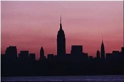 A distant skyline of entirely dark skyscrapers against a sunset pink sky.