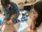 A photo showing two students placing amino acid models onto a cord so they can construct a model polypeptide and then test its cohesive properties with a force probe.
